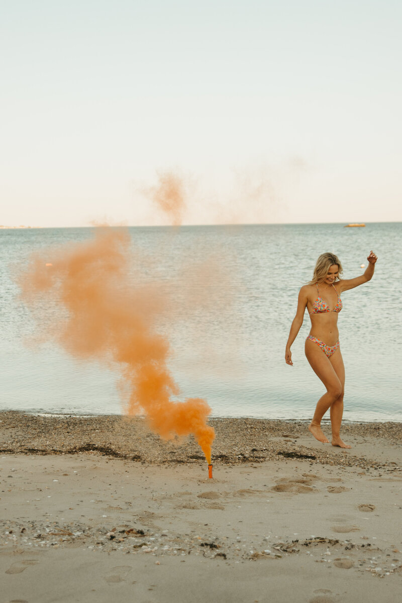 Girl in bikini on beach with orange firecracker