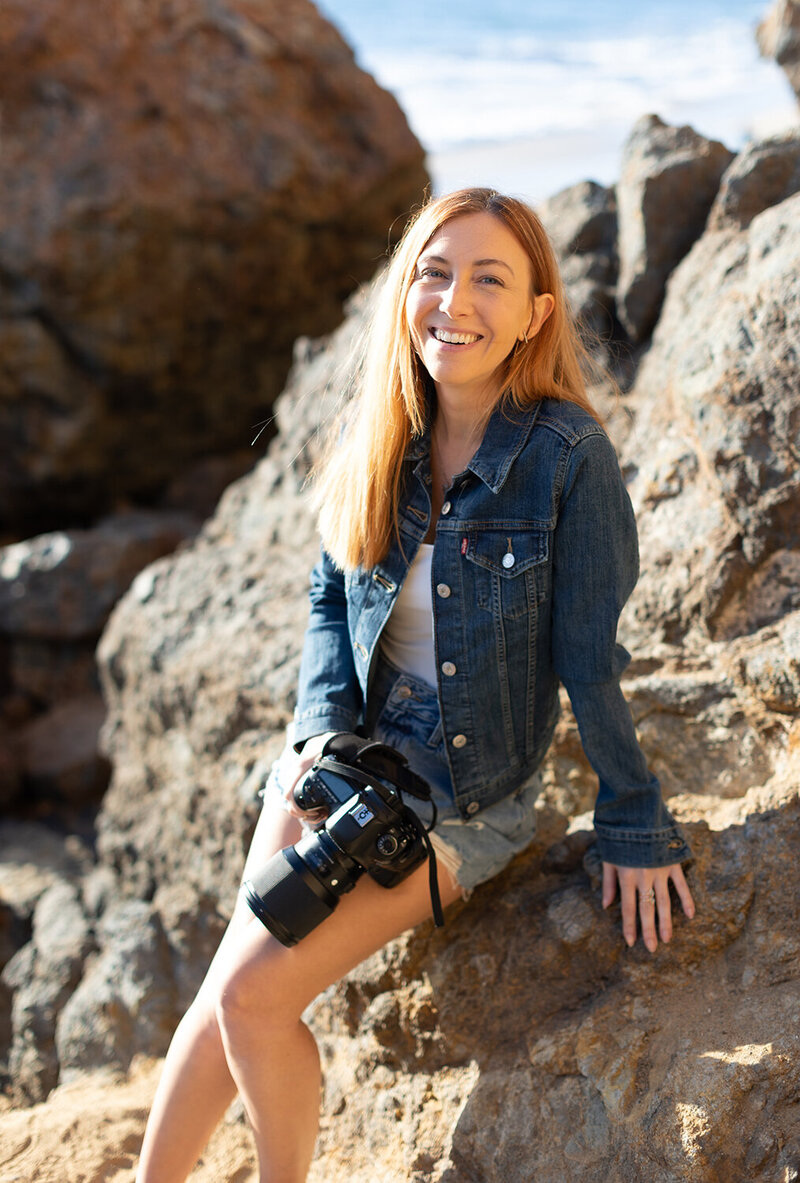 woman sits on a rock with a camera