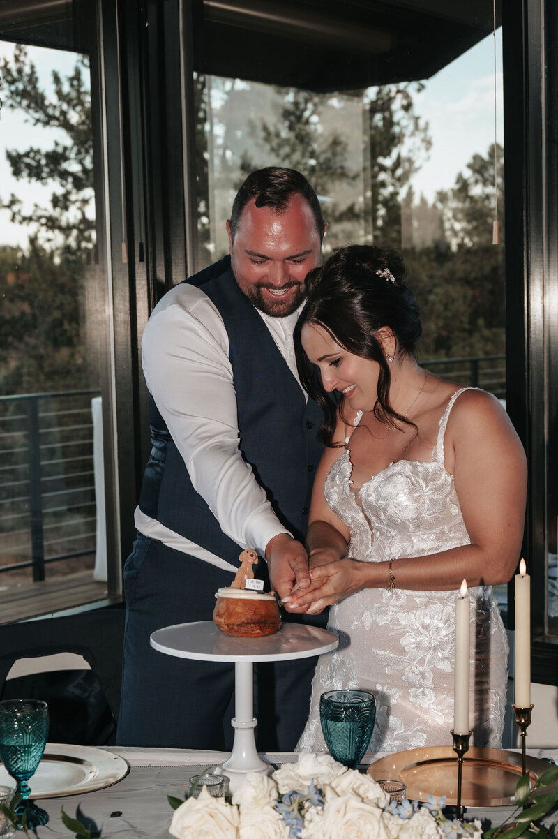 Couple in wedding attire sharing an intimate moment while cutting their wedding cake during an elegant reception at River Run Lodge.