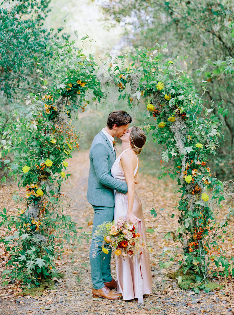 Bride and groom kiss during a colorful autumn wedding ceremony in the forest