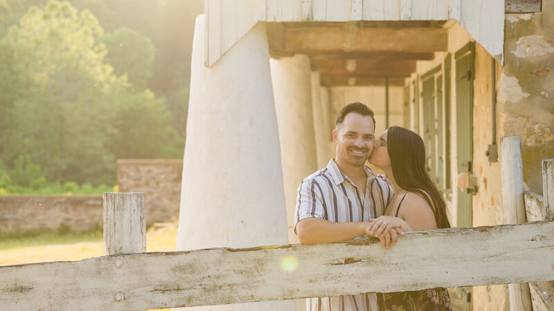 Couple snuggling near a barn during golden hour at Valley Forge National Historical Park, framed by warm light.