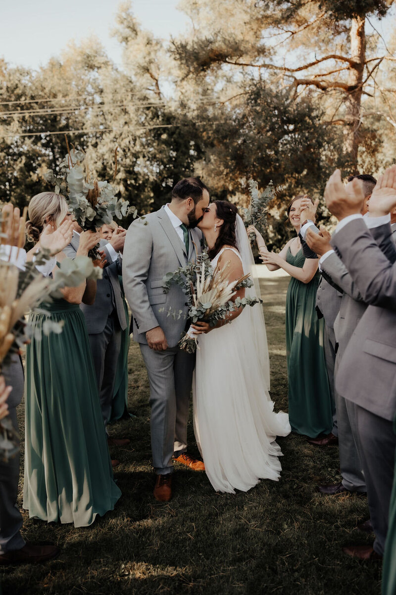 Newlyweds kissing with wedding party clapping