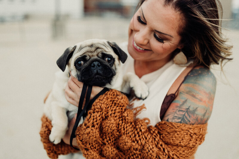 Kate holds Dennis the pug and smiles at him.