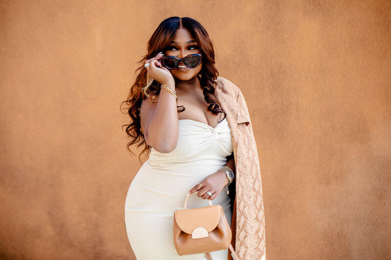 A chic Black content creator strikes a pose in a beige tube dress against a tan wall. This lifestyle portrait highlights her bold fashion sense and creative spirit, perfect for social media and branding.