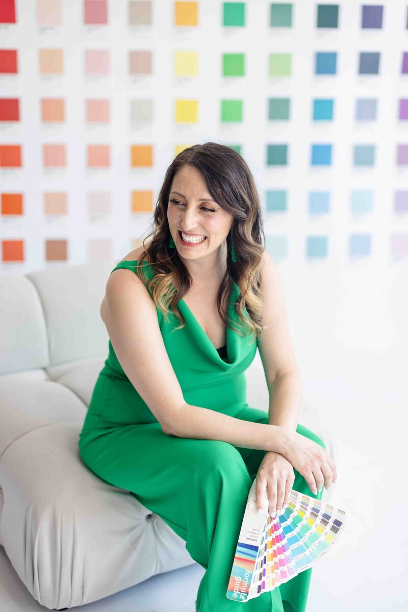 Color psychology expert in emerald green dress reviewing Pantone color swatches during strategic brand palette development session