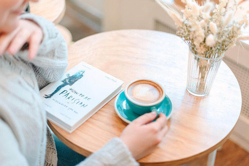 Rachael Laporte, Paris Photographer, sitting at table with coffee, book and vase of flowers