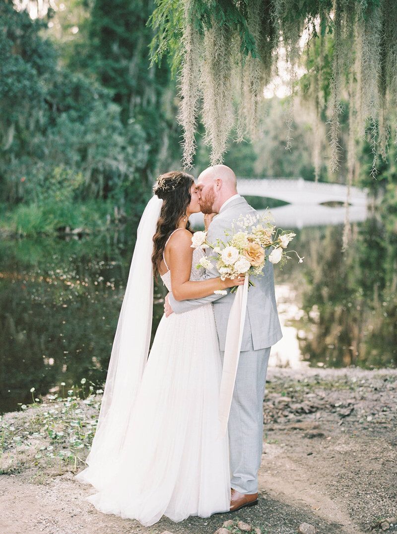 Bride and groom kissing in front of a pond under spanish moss