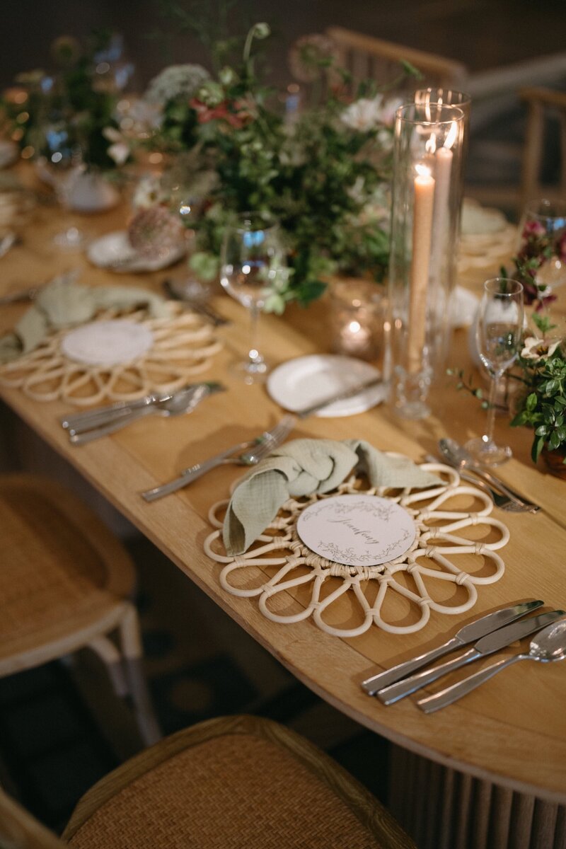 Elegant table setting with a sunburst placemat, folded napkin, and floral arrangement, illuminated by candles.