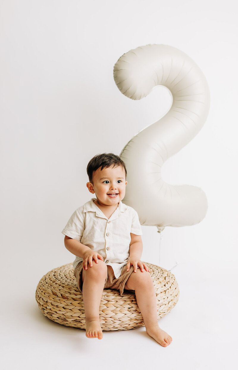 Photo of a 2 year old boy with a large 40" number two balloon in the background in an all white studio setup