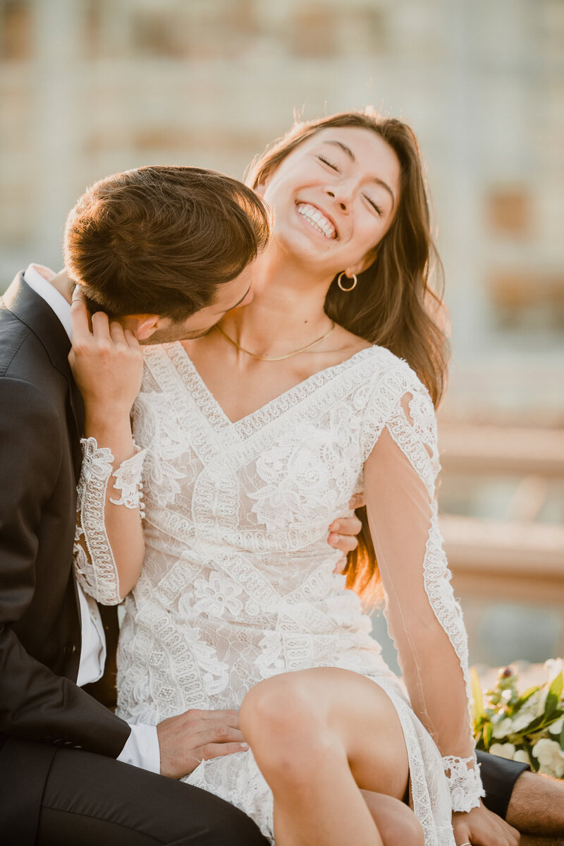 Groom kisses bride’s neck as she laughs in golden-hour light on a New York City rooftop, captured by NYC wedding photographer Heritage House.