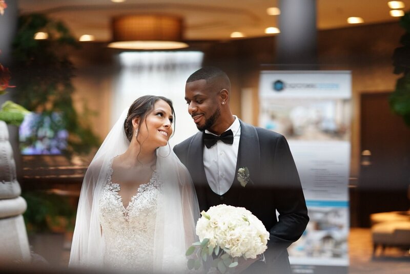 A wedding couple strolls through a chic urban setting, captured creatively through window blinds for a cinematic feel. This image highlights the artistic approach of our wedding videography service, showcasing how we blend modern elegance with storytelling to create visually stunning wedding films.