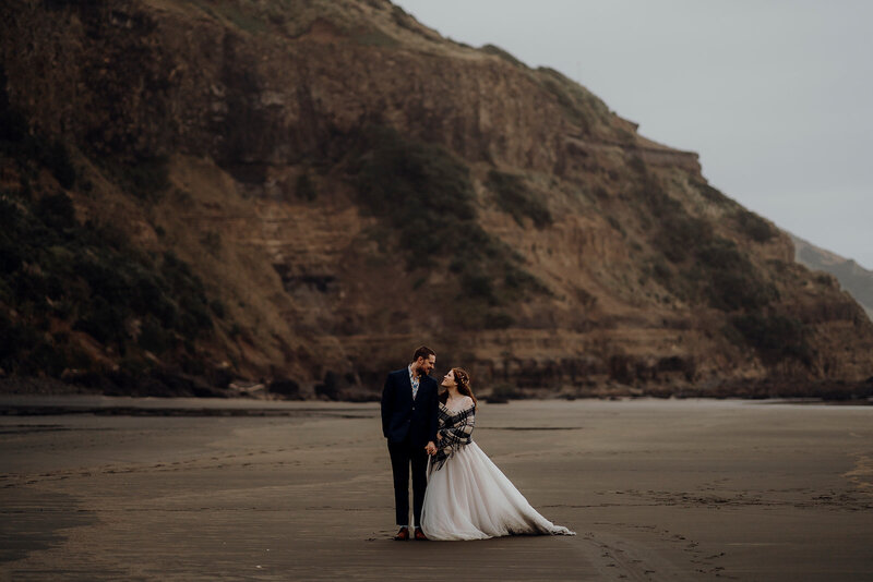 A bride and groom standing on the dark sand in Muriwai during an elopement wedding photoshoot with waikato photographer Haley Adele Photography