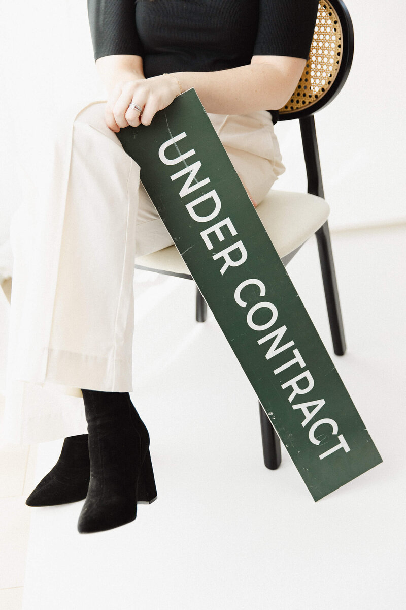 Person Seated holding an 'Under Contract' Sign