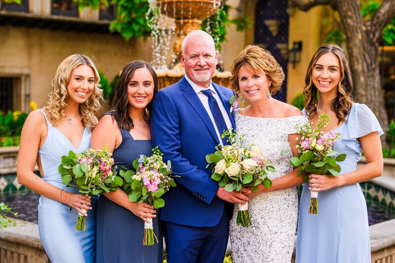 Bride and groom with their children smiling and looking at camera holding bouquets with fountain background for elopement at Tlaquepaque in Sedona Arizona
