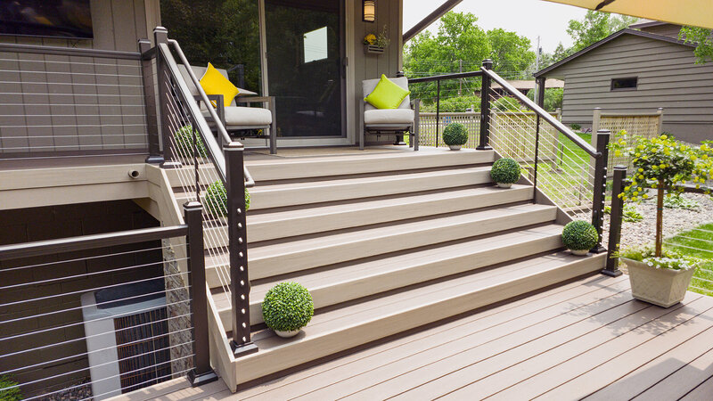 An extra-wide staircase with cable railing and accented with small round boxwood topiaries. 
