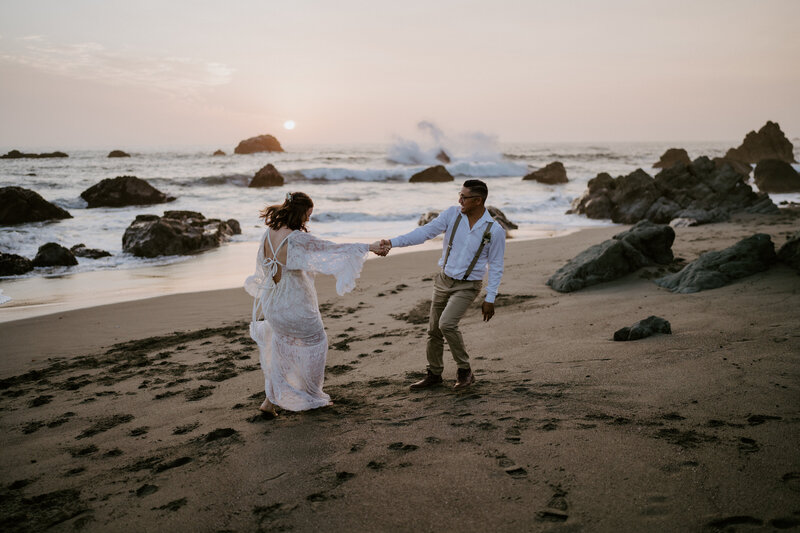bride and groom holding hands running on beach