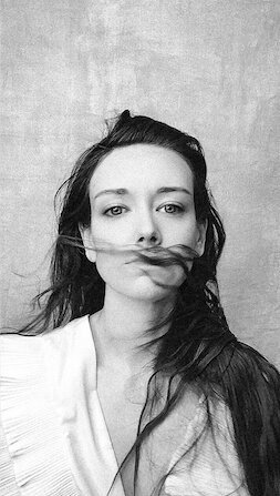 black and white studio headshot of a woman looking a the camera with her hair blowing in front of her face