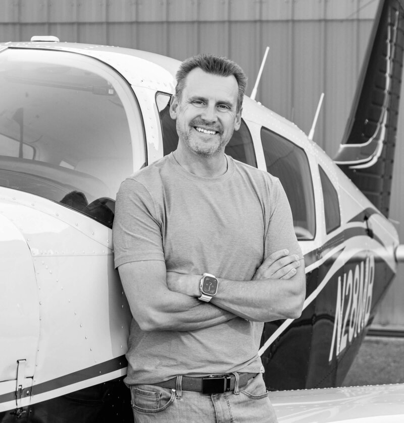 Lon Stroschein standing confidently beside a small private airplane, embracing life after corporate reinvention