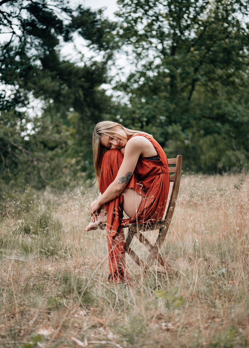 Frau im roten Kleid sitzt auf einem Stuhl in der Lüneburger Heide und umarmt sich voller Selbstliebe