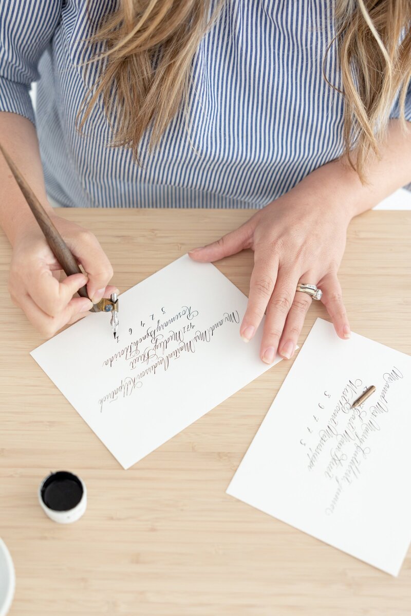 Woman writing pointed pen calligraphy on white envelopes.