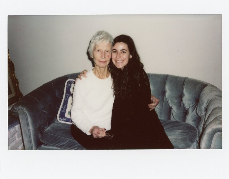 Polaroid of an older and younger woman hugging and smiling at camera while sitting on a blue tufted couch