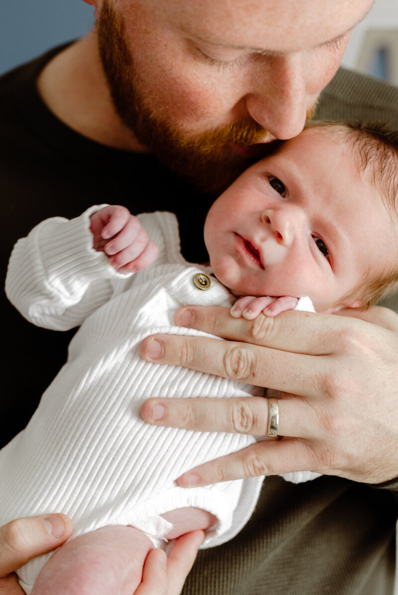 Dad is holding baby and kissing him on the head