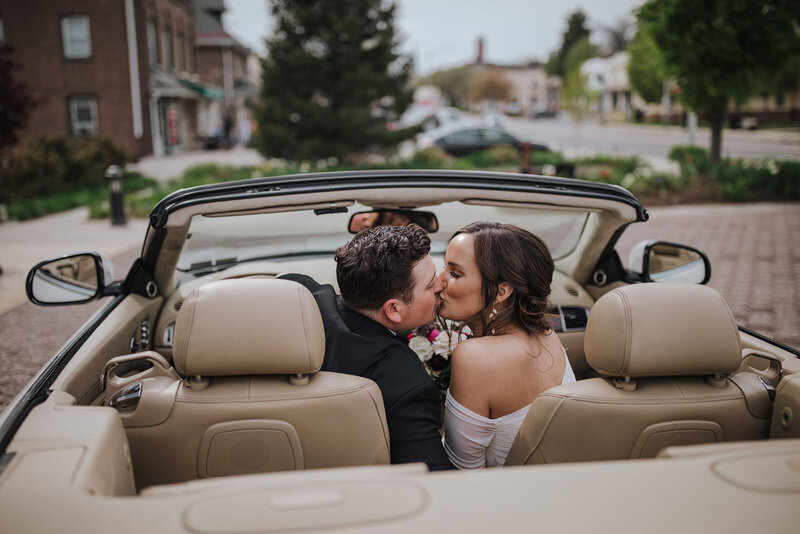 A couple kissing while sitting in the front seat of a convertible