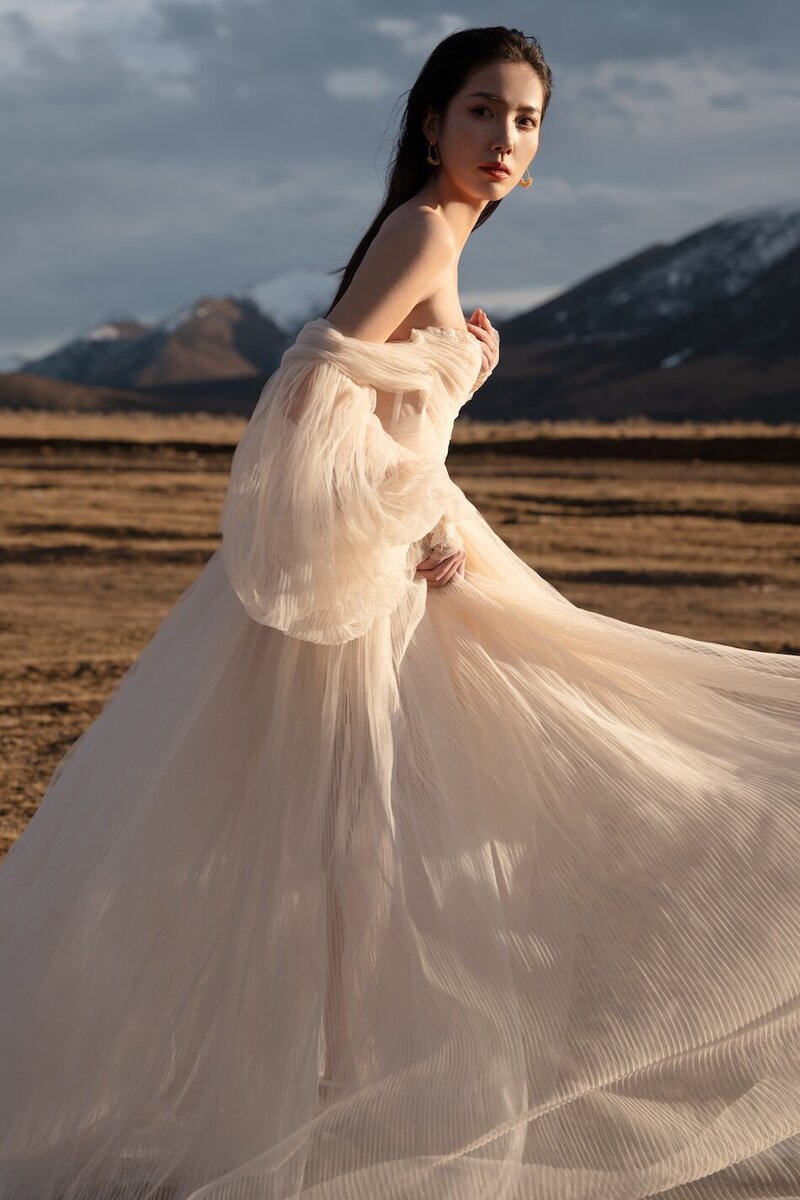 Couture dress bridal shoot on a field with mountains in the background and golden light.