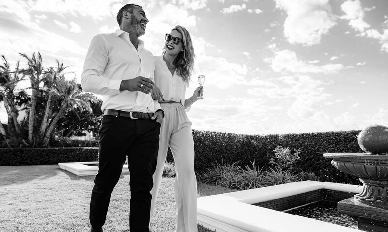 Couple laughing together outside in garden. The wife holds champagne in a glass