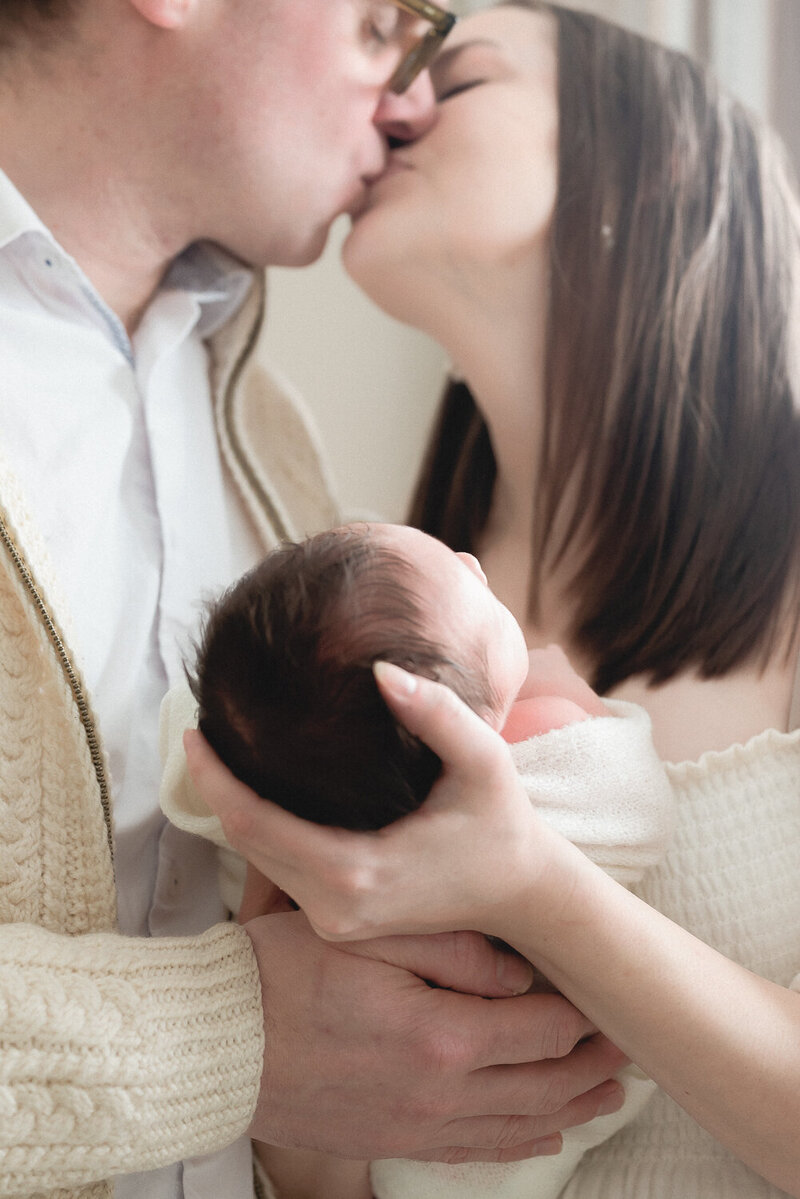 Couple kissing while holding newborn