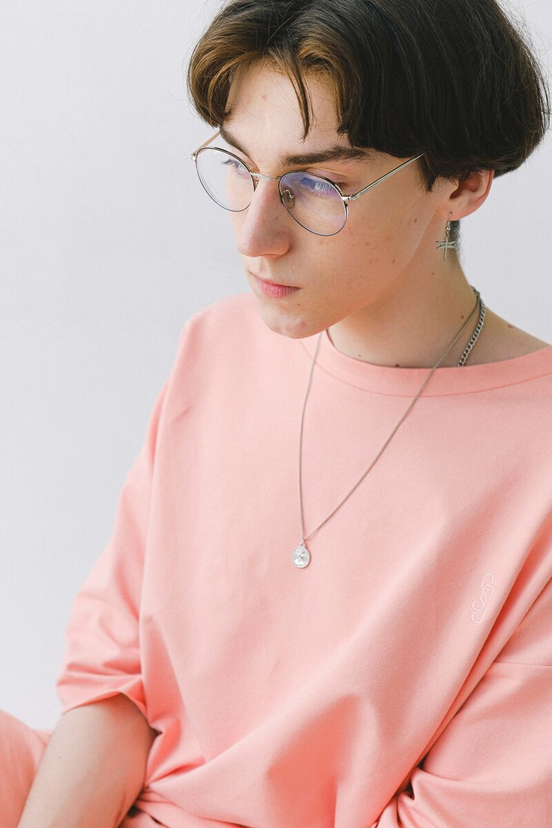 A teen wearing glasses and jewelry looks past the camera. They have a frustrated expression on their face, eyes looking over their shoulder.