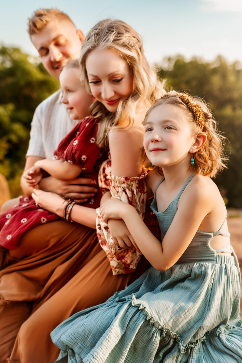 Family snuggles and links arms in beautiful dresses on a rock at Elephant Rocks Park in Missour during a Kansas City LIfestyle Photogrphy session