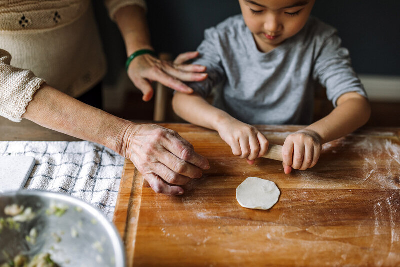 grandma's hands gently touching grandson as uses rolling pin with dough to make homemade dumplings