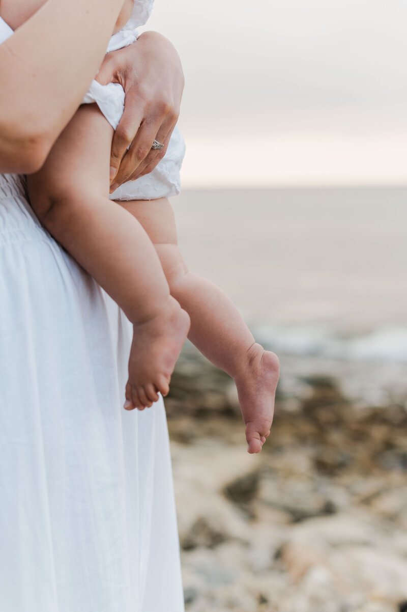 A close up photo of a mother holding her young child at the beach, focusing on the little girls cute feet.