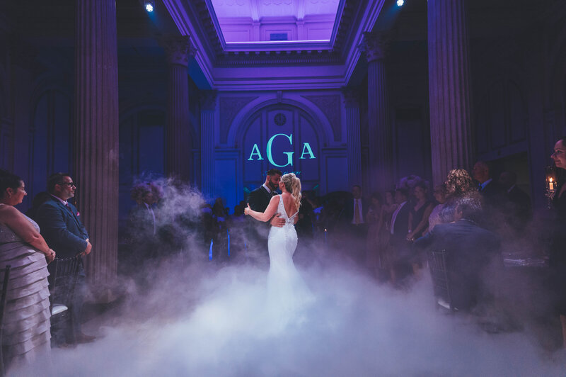 A bride and groom are dancing with fog surrounding them with purple lighting behind them