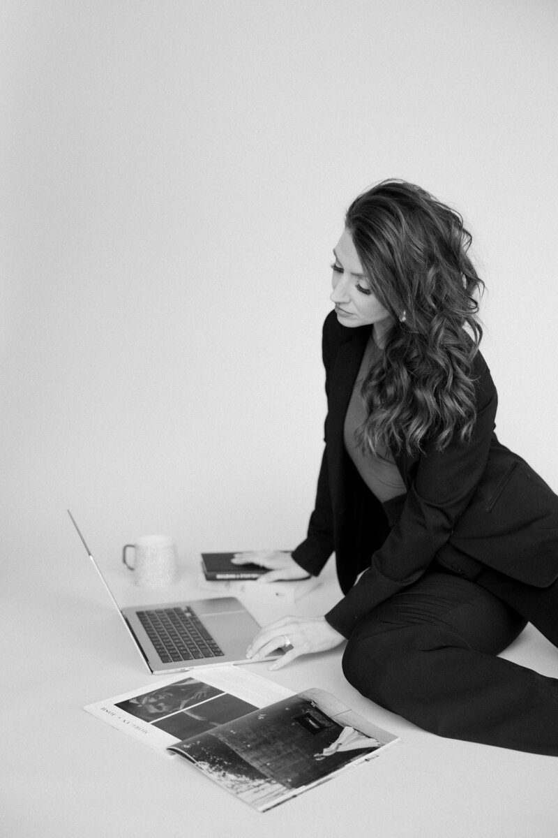 Black and white headshot of promise bridal artistry sitting on the floor with her laptop 