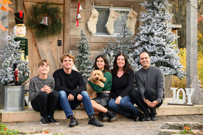 family of five with mom and dad, two boys and a daughter with their puppy sitting in front of a cabin for the family Christmas Photos in Burlington, Ontario.
