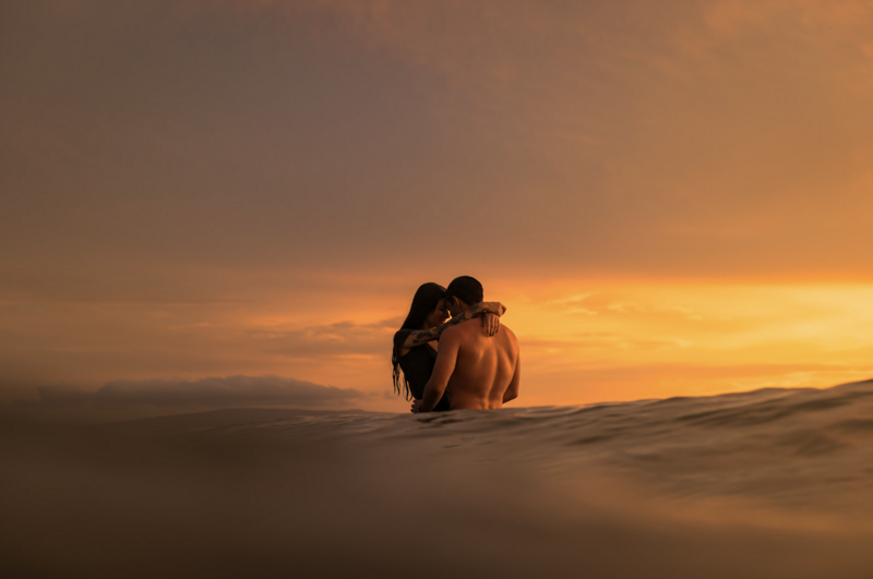 couple in the ocean at sunset embracing with the glowng ocean surrounding them
