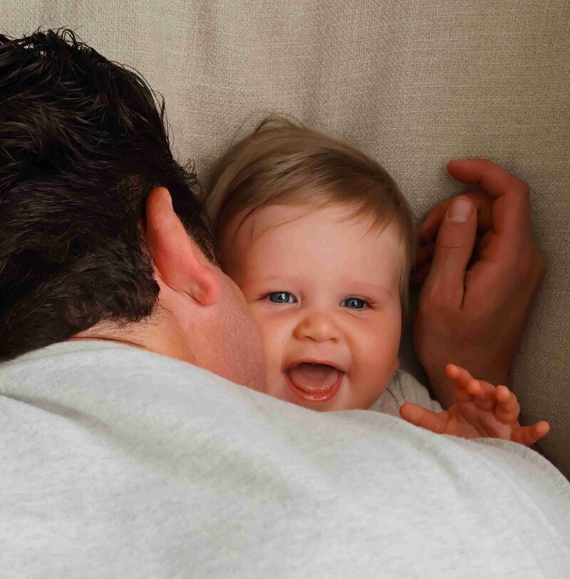 A dad lovingly kisses his smiling baby on the cheek, showcasing a tender moment between father and child.