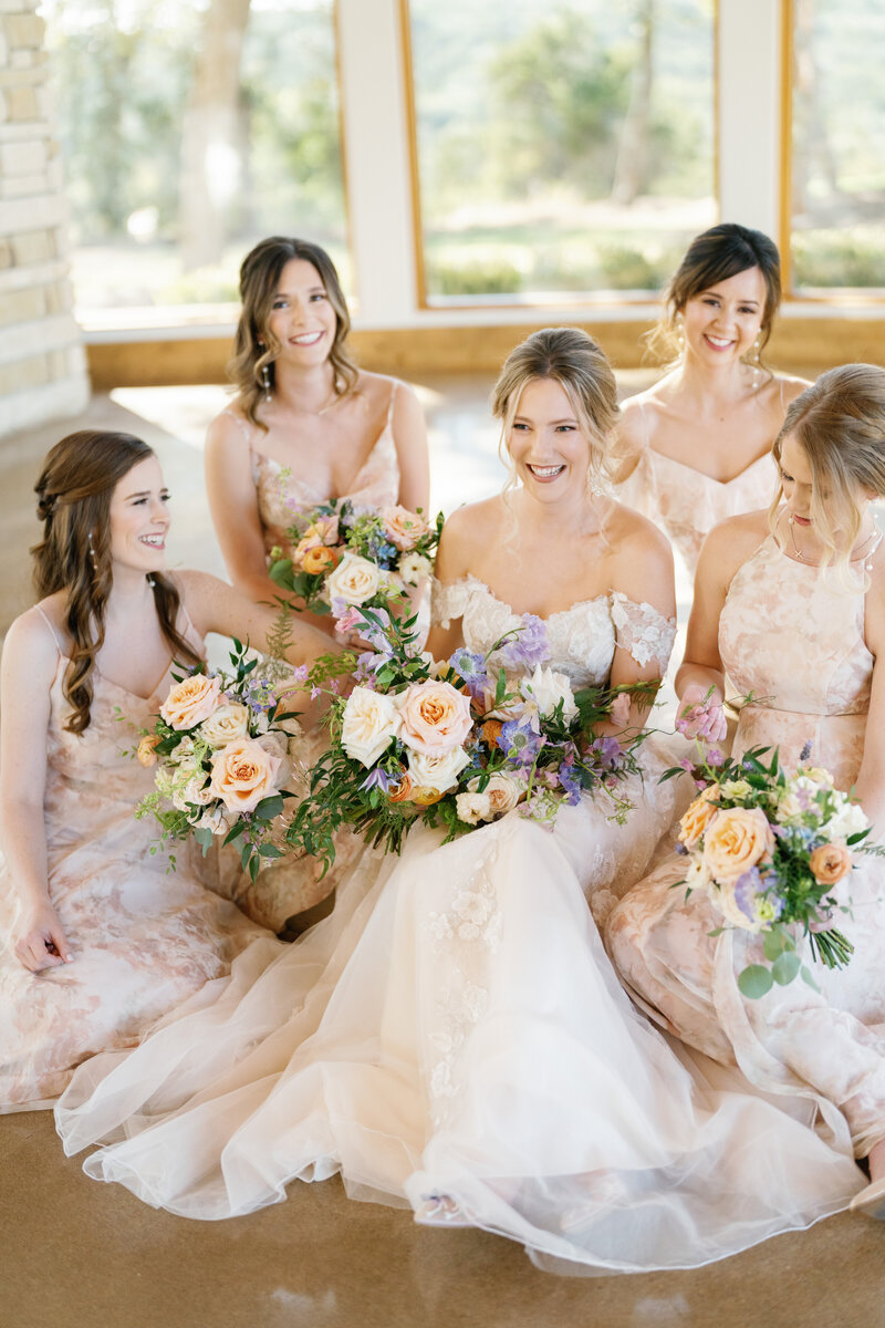Bride sitting on the floor surrounded by her bridesmaids in pink dresses