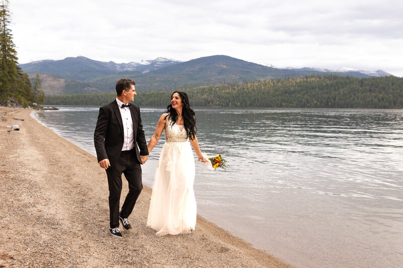 Bride and Groom walking hand in had on lake shore smiling at each other