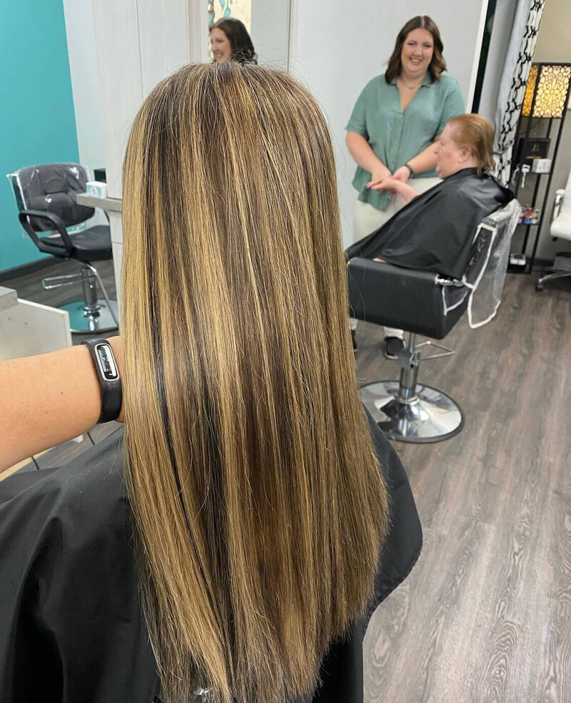 A back view of a woman with long, sleek, straight hair, showcasing a smooth and polished look created by 212 Salon, Spa, & Barbershop.