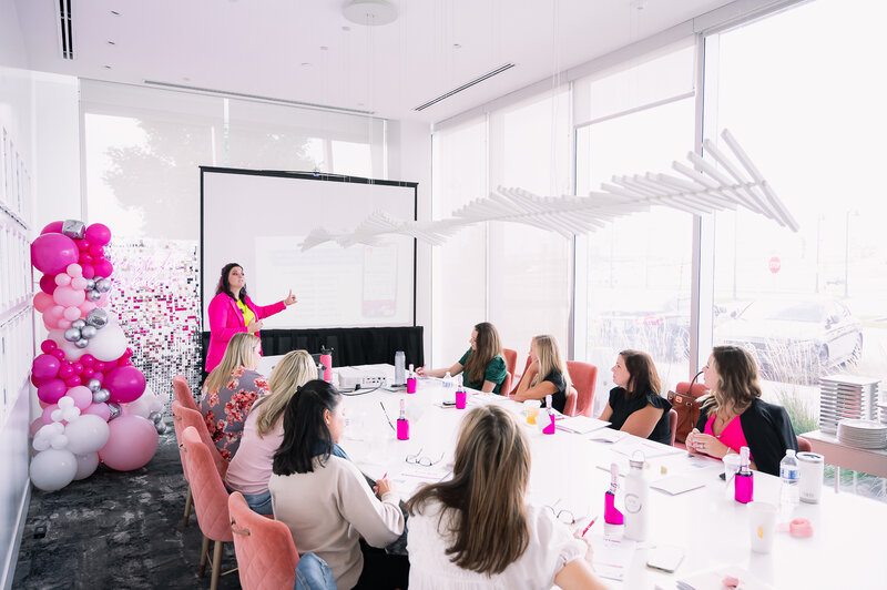 Jessi Cabanin holding a pink planner notebook sitting at a desk with a laptop and boss babe coffee cup on it.