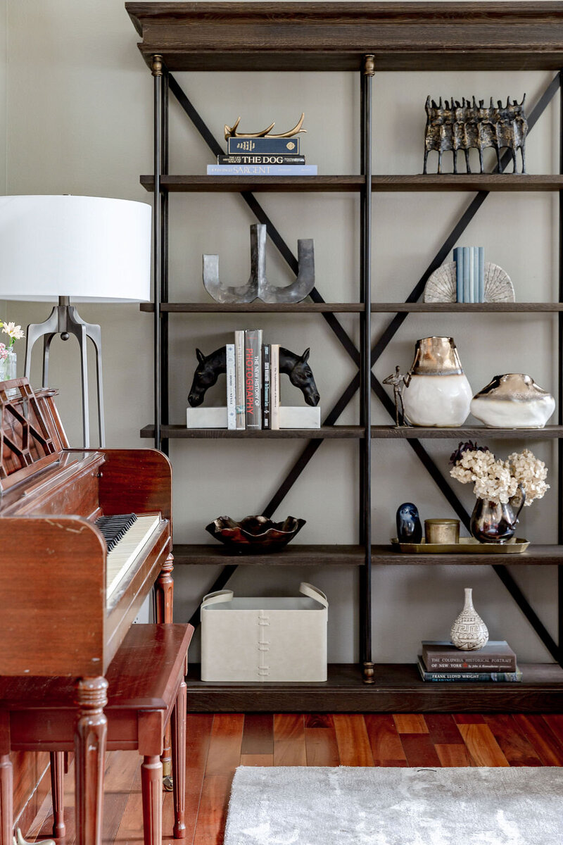 Wooden shelving with collectibles with a upright piano next to it.