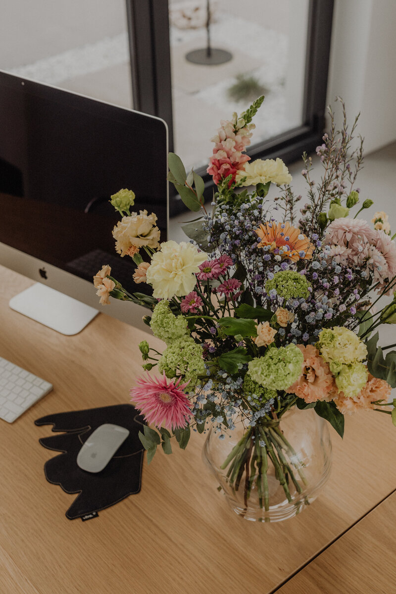 A bright workspace with a computer and colorful bouquet of flowers — styled office image for The Veiled Method™ Bio Boss™ sales page.