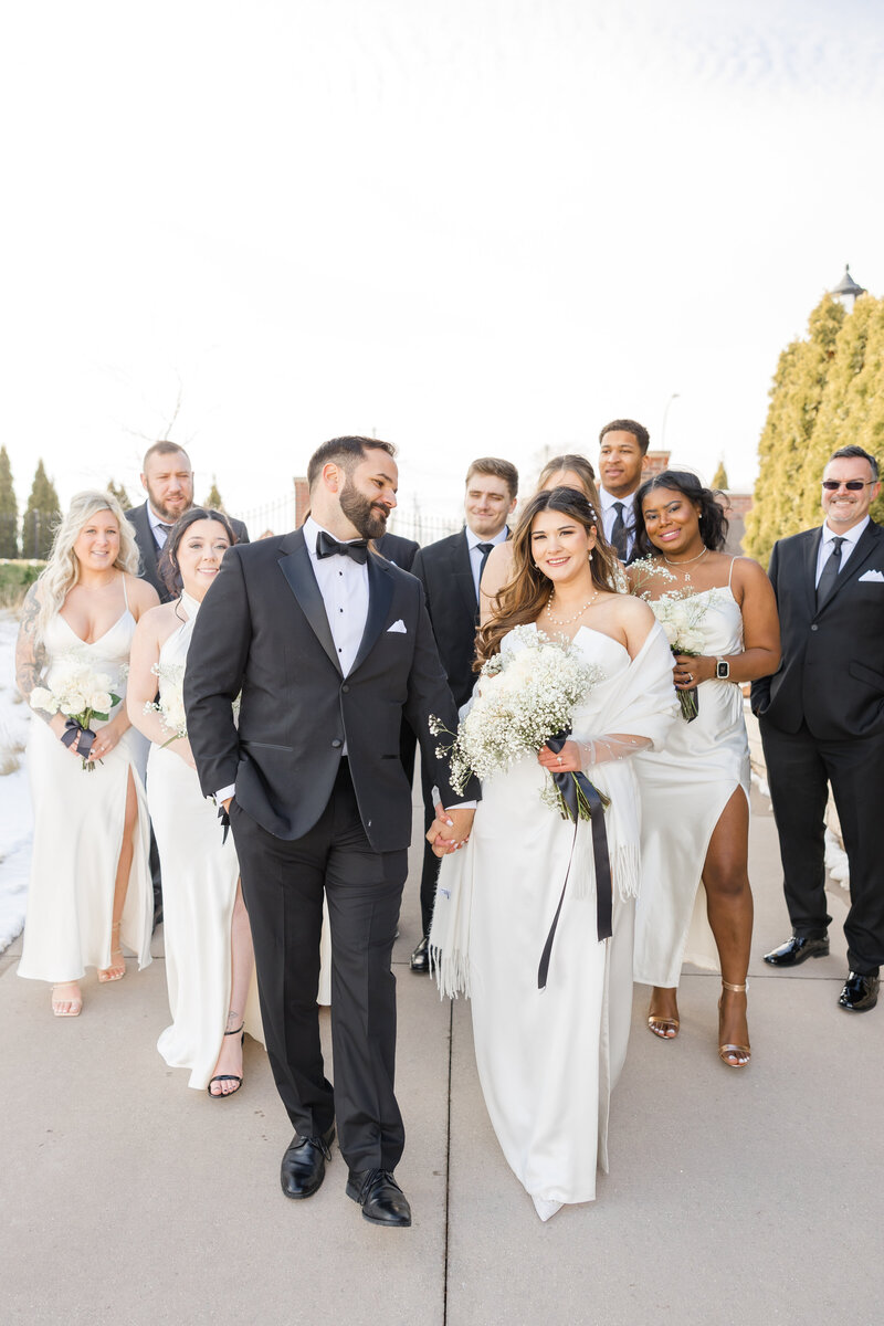 A groom in a black suit nuzzles his bride while standing on a wooden dock in Saginaw Michigan