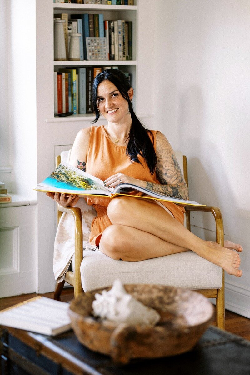 jackie seating in a chair smiling in a camera while flipping a magazine