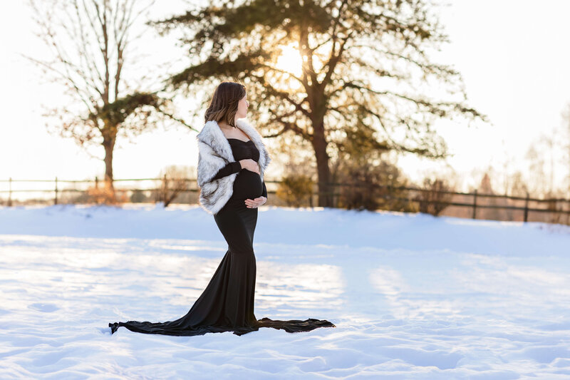 A pregnant woman posing in a snowy field at sunset in Fairfax County, Virginia.
