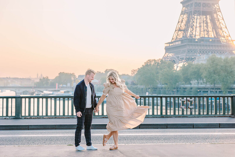 Man and woman holding hands near the Eiffel Tower at Bir-Hakeim Bridge during a romantic Paris couples photoshoot, with the woman wearing a dress.