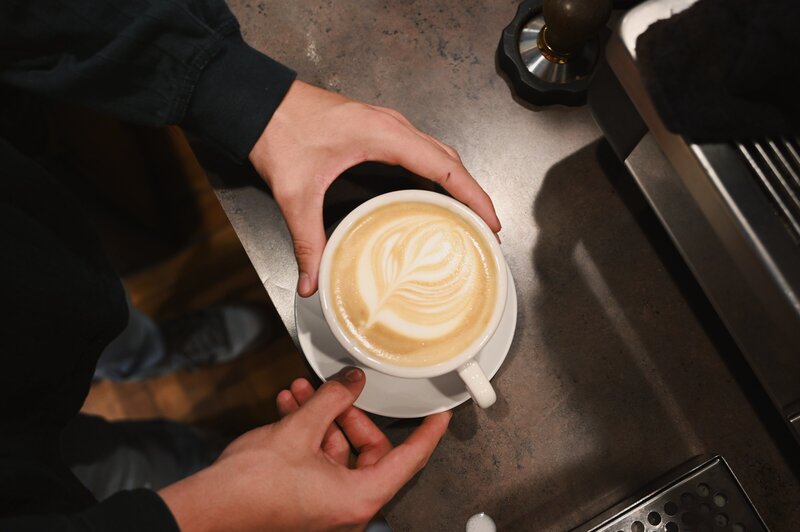 Barista holds a white ceramic cup  and plate with latte art